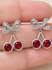 Both cherry bow drop earrings held in an open palm showing scale and red crystal detail