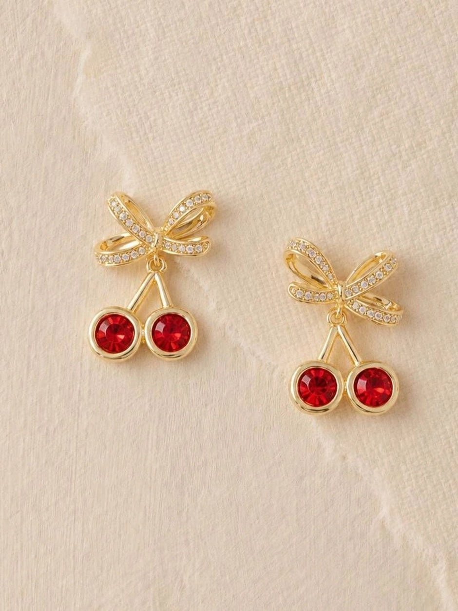 Two cherry crystal drop stud earrings displayed on a light textured fabric surface