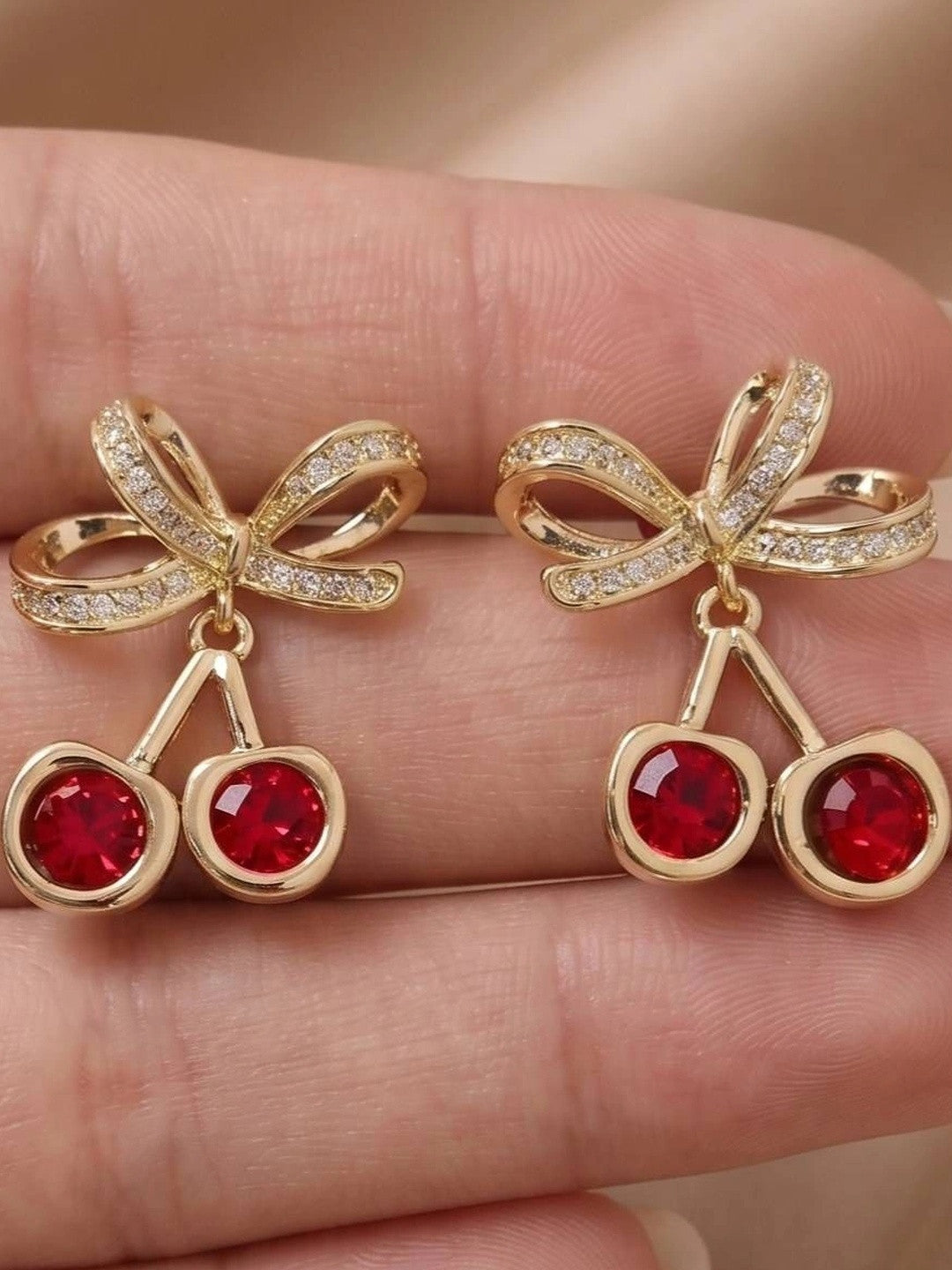 Close-up of cherry crystal drop studs held in a hand showing red crystal and bow detail