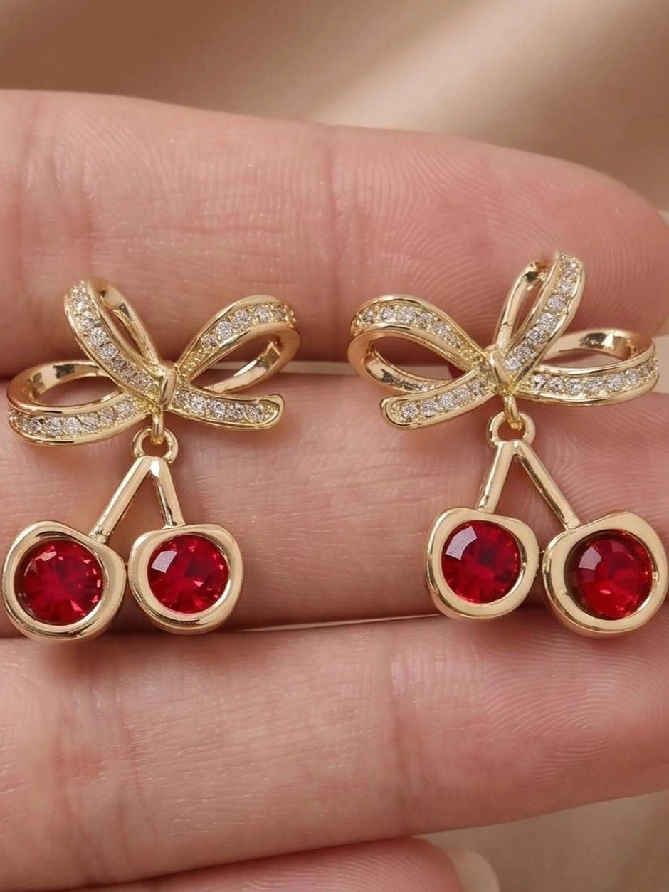 Close-up of cherry crystal drop studs held in a hand showing red crystal and bow detail
