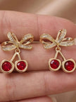 Close-up of cherry crystal drop studs held in a hand showing red crystal and bow detail