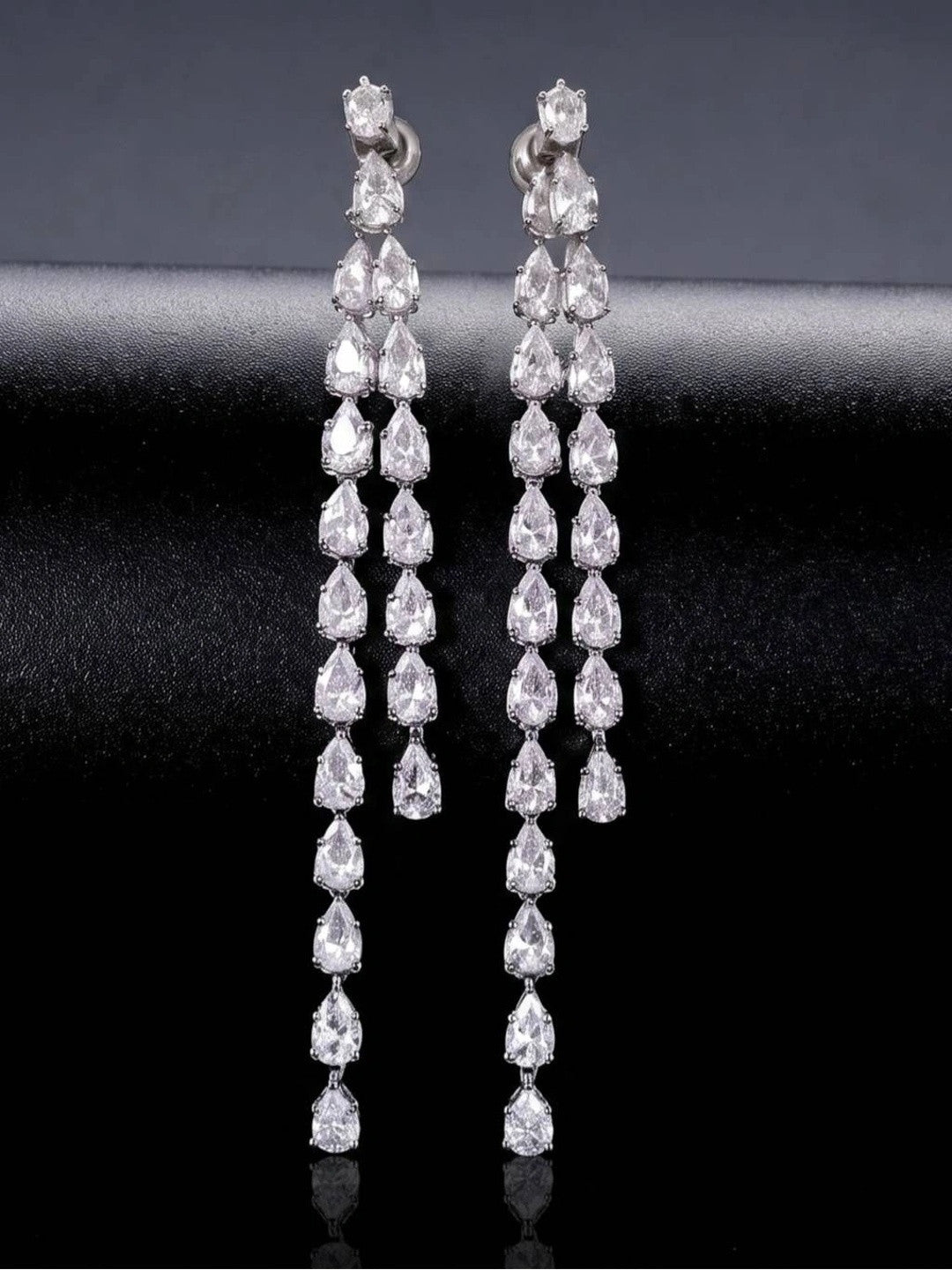 Pair of long silver CZ teardrop drop earrings displayed upright against dark fabric