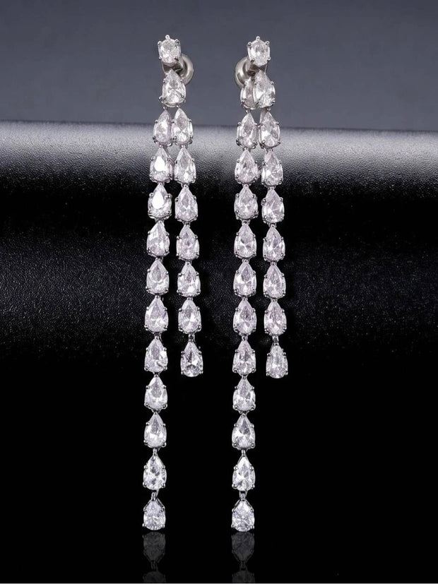 Pair of long silver CZ teardrop drop earrings displayed upright against dark fabric