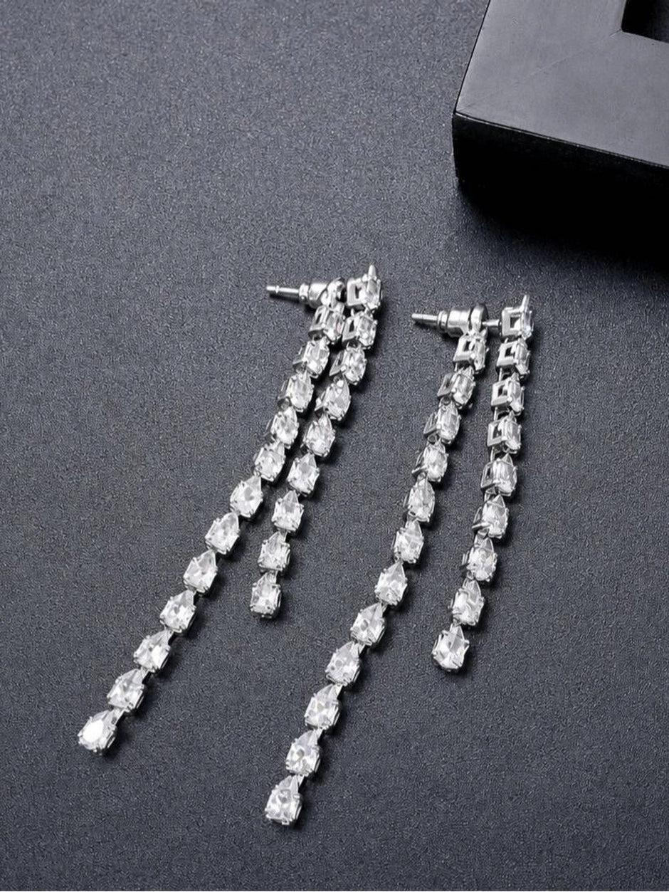 Two silver CZ drop earrings laid flat beside a black gift box on grey surface