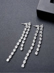 Two silver CZ drop earrings laid flat beside a black gift box on grey surface