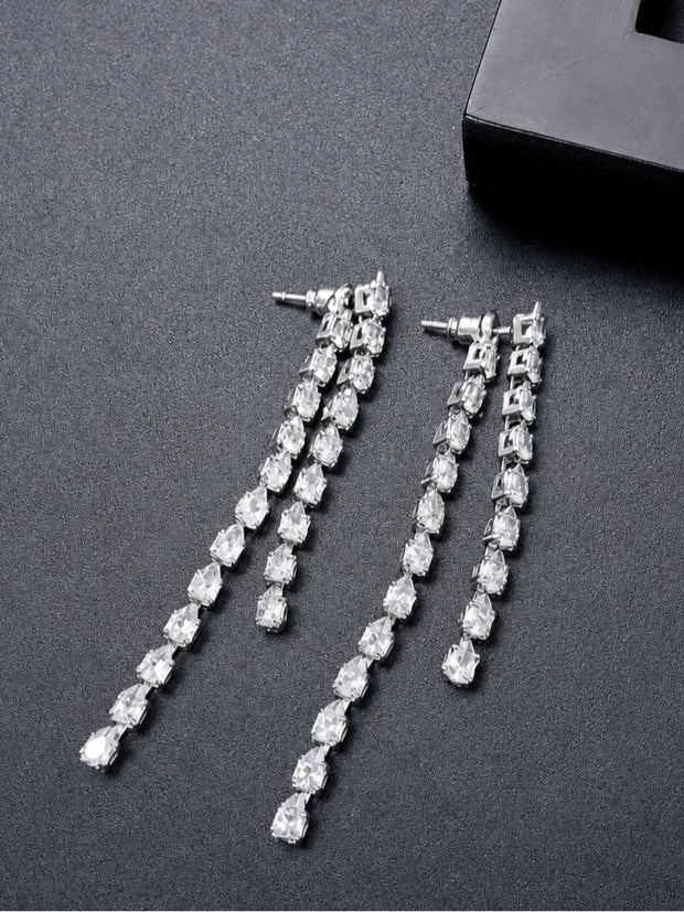 Two silver CZ drop earrings laid flat beside a black gift box on grey surface