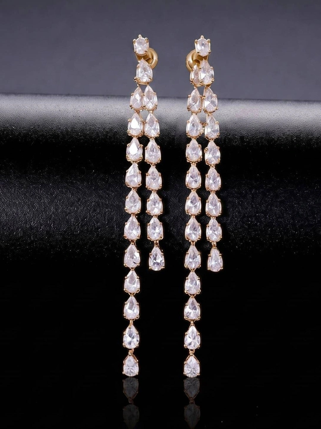 Front view of both gold-plated pear-cut CZ drop earrings standing upright on black satin surface