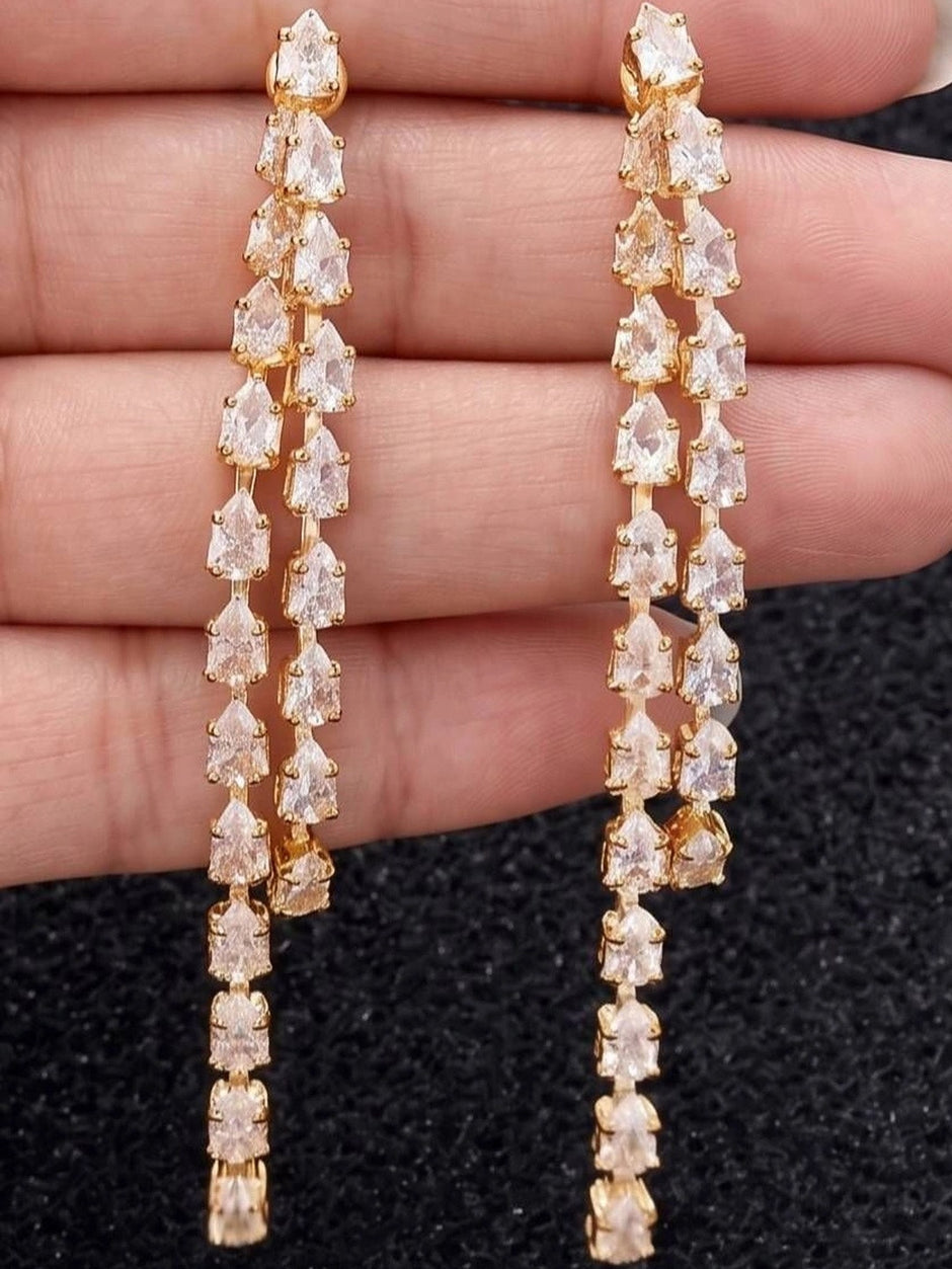 Close-up of gold-plated CZ teardrop earrings held in an open palm showing dual-strand stone detail
