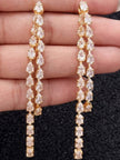 Close-up of gold-plated CZ teardrop earrings held in an open palm showing dual-strand stone detail