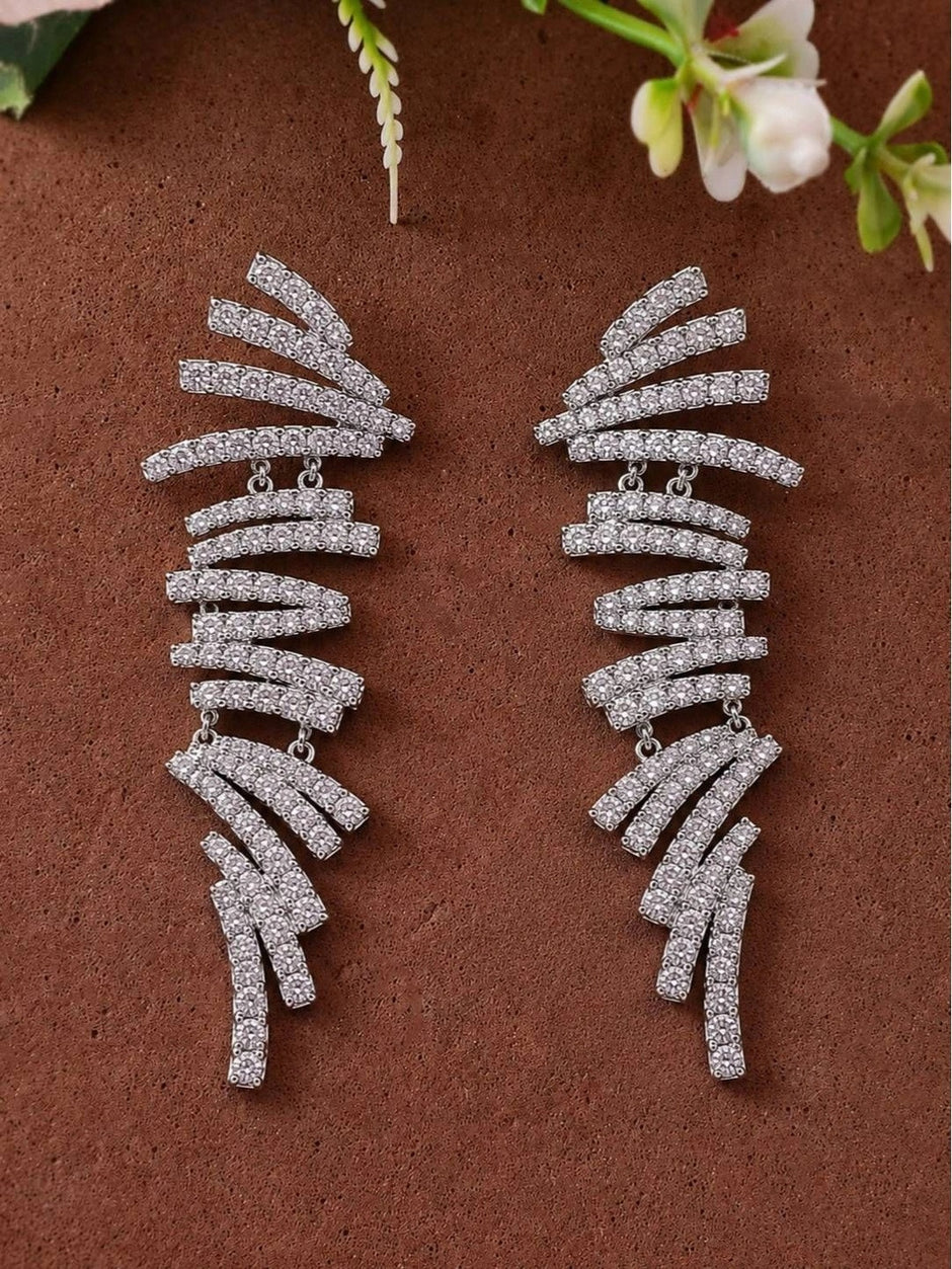 Pair of silver CZ spiral bar drop earrings laid flat on a terracotta surface with white flowers