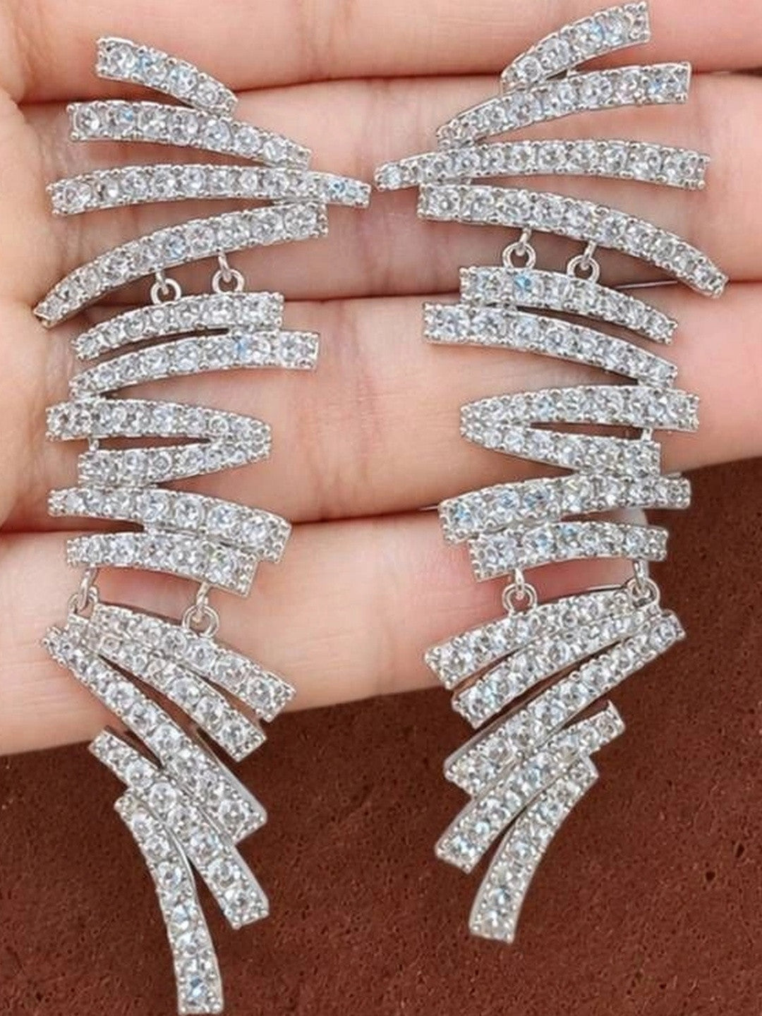 Close-up of both CZ spiral bar earrings held in a palm showing full length and layered bar detail