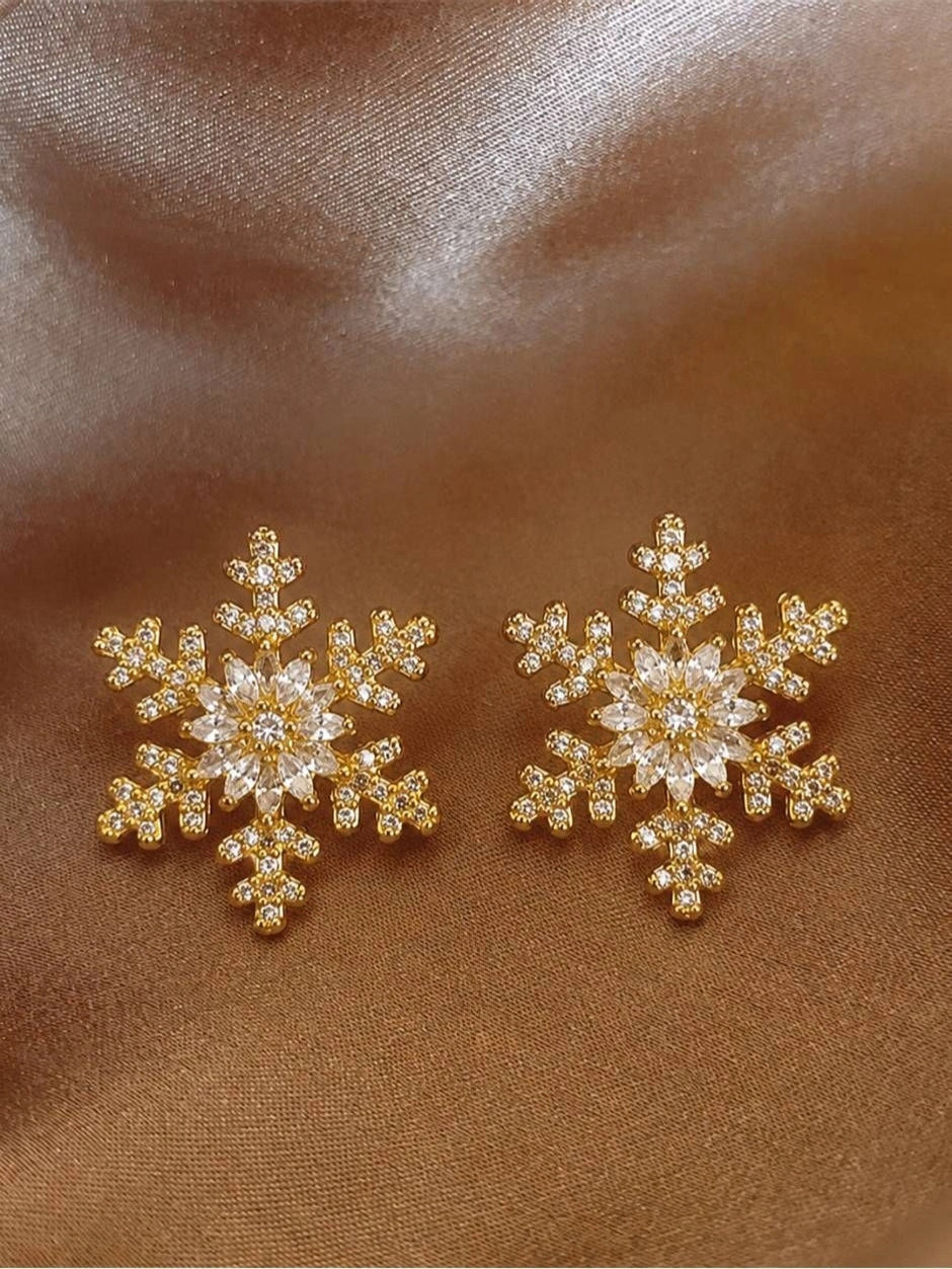 Pair of gold-plated snowflake stud earrings with cubic zirconia centre laid flat on brown satin