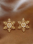 Pair of gold-plated snowflake stud earrings with cubic zirconia centre laid flat on brown satin
