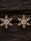 Two gold snowflake CZ stud earrings displayed on dark textured wood surface