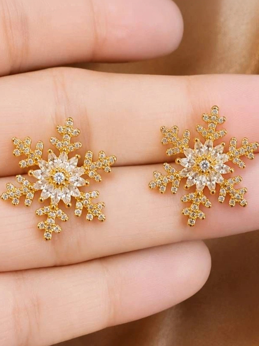 Close-up of gold snowflake stud earrings with marquise cubic zirconia held in a woman's palm