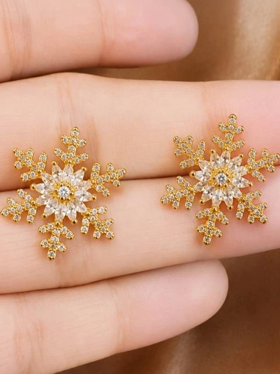 Close-up of gold snowflake stud earrings with marquise cubic zirconia held in a woman's palm
