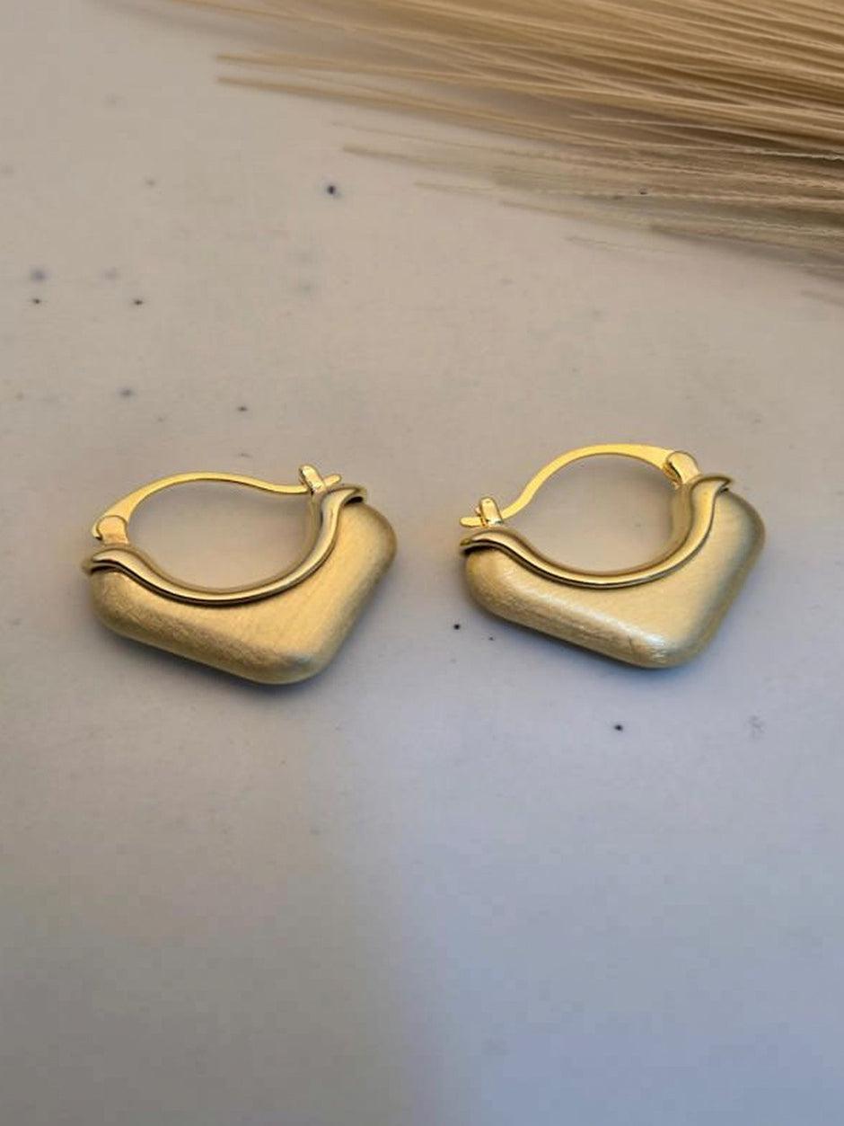 Pair of gold-plated chunky square hoop earrings with brushed matte finish on white marble surface