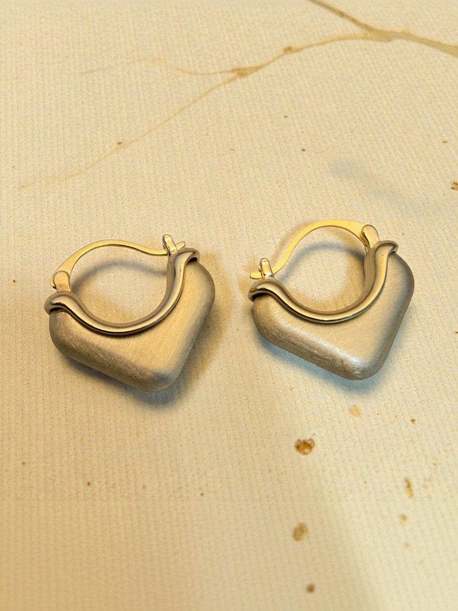 Two gold-tone square hoop earrings with click-top clasp laid flat on beige textured background