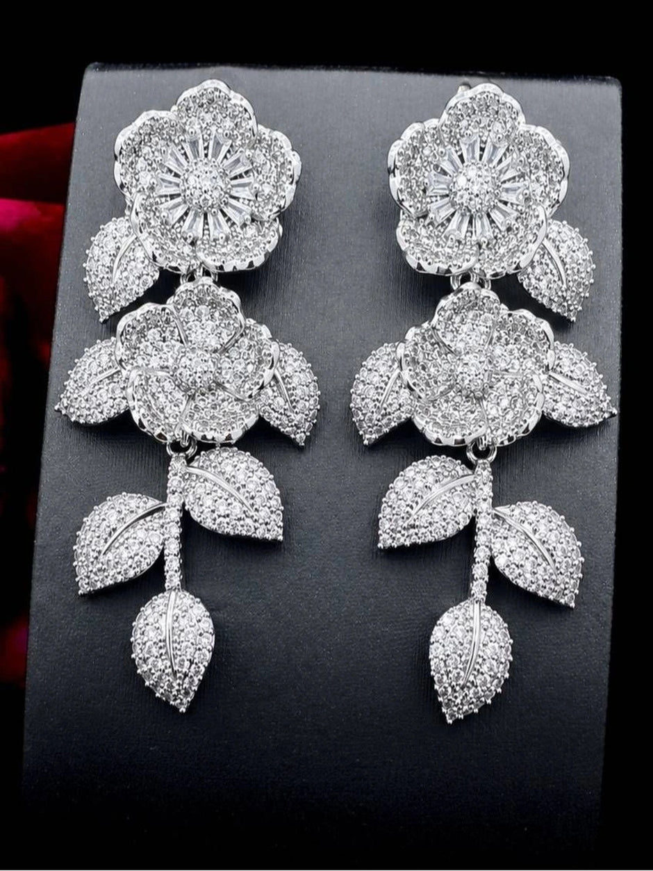 Pair of silver CZ floral drop earrings displayed upright on a dark jewellery stand