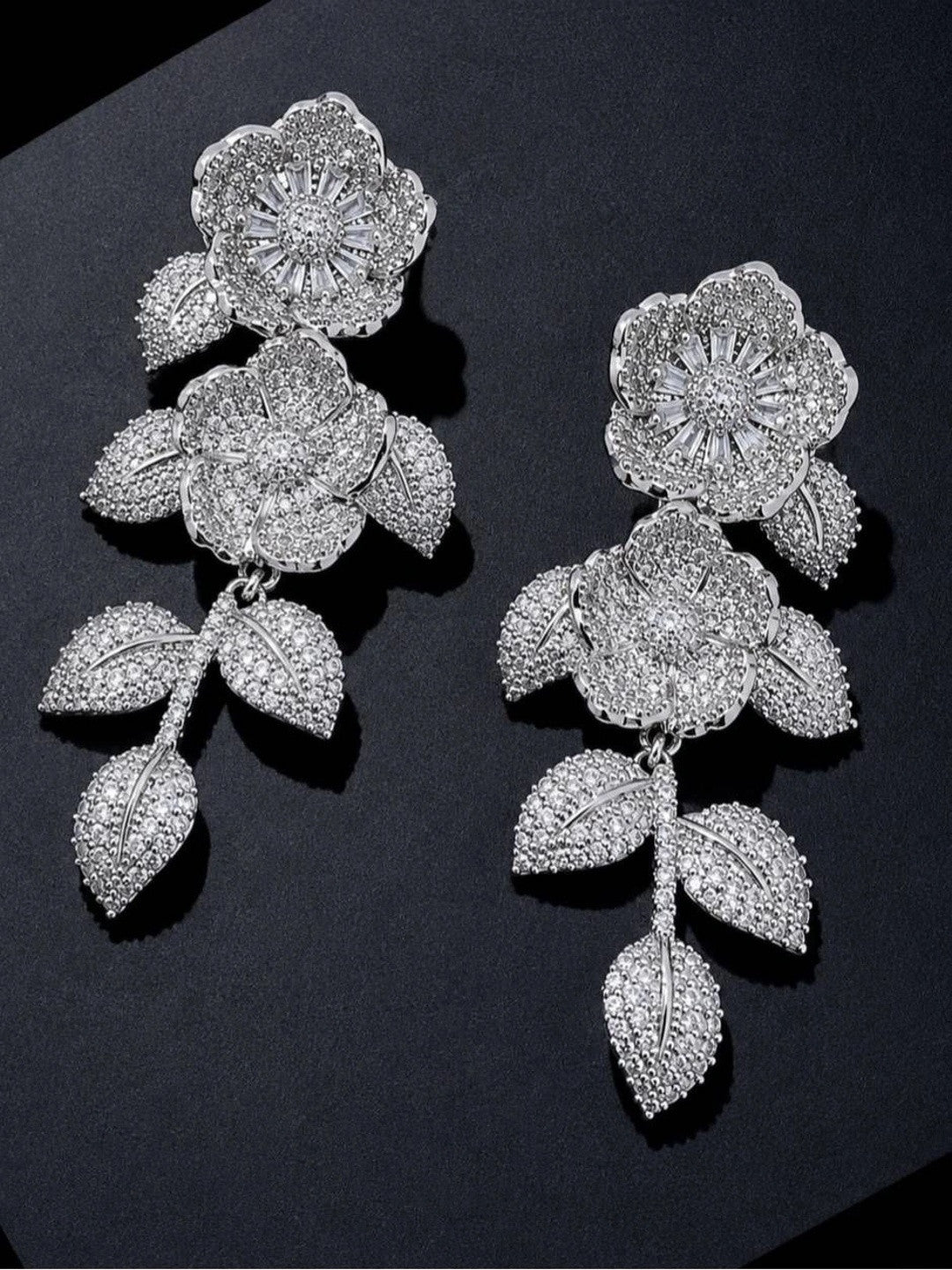 Two silver pavé CZ floral earrings laid flat on a dark surface showing full drop length