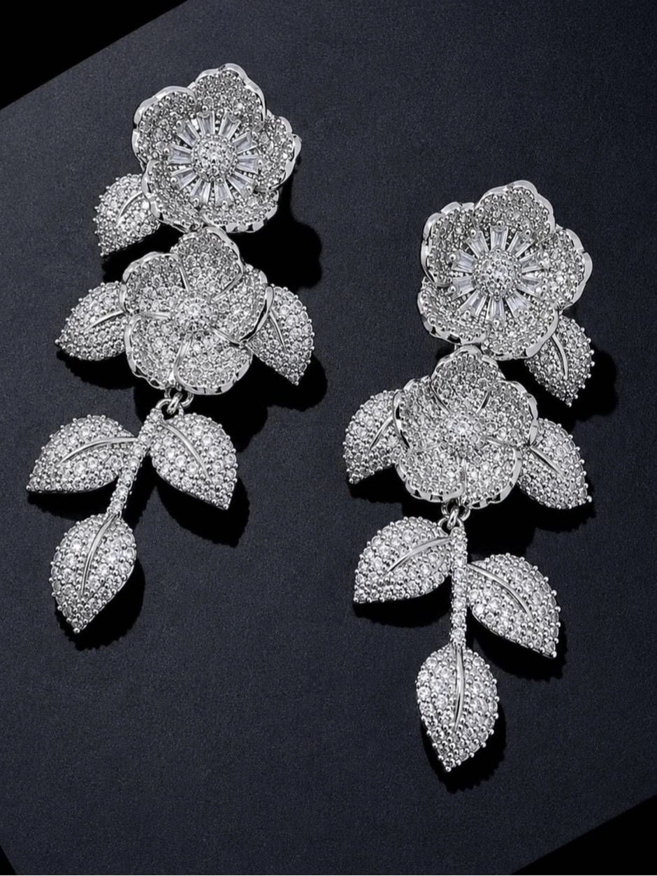 Two silver pavé CZ floral earrings laid flat on a dark surface showing full drop length