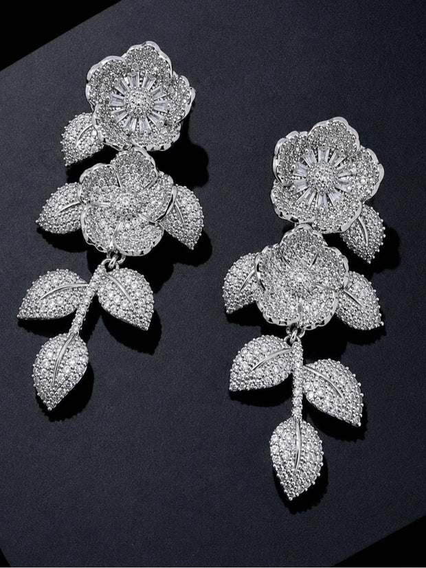 Two silver pavé CZ floral earrings laid flat on a dark surface showing full drop length
