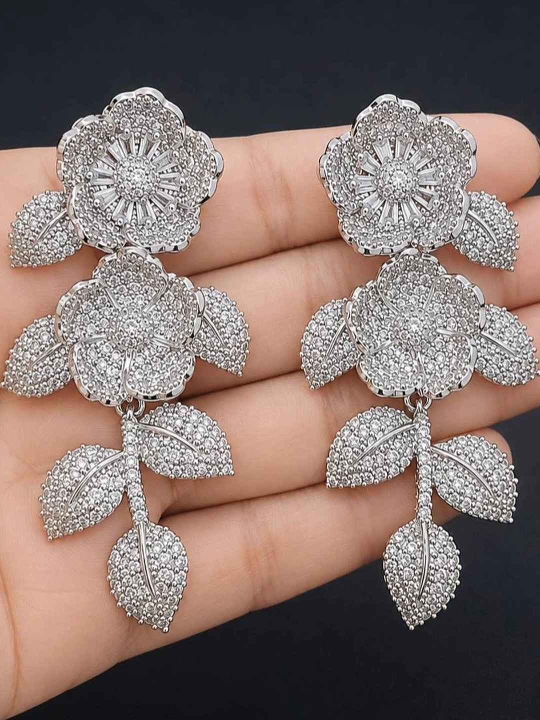 Pair of large silver CZ floral drop earrings held in an open palm for size reference