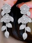 Silver CZ floral drop earrings held near a model's ear showing wearable drape and scale