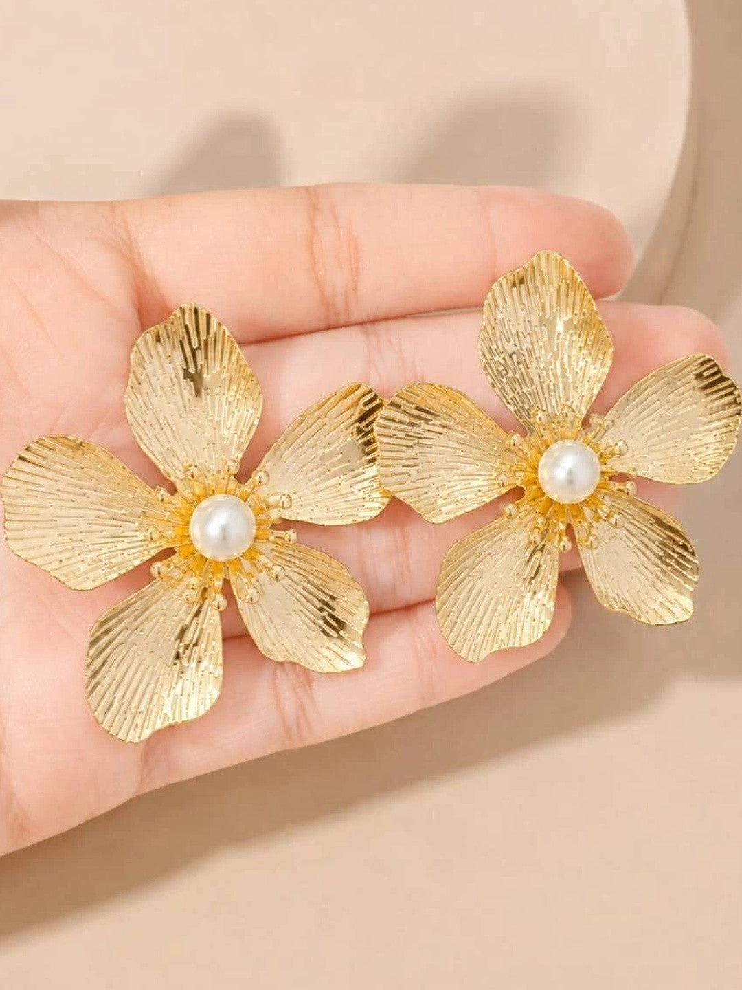 Close-up of gold floral stud earrings with pearl centres resting in an open palm showing petal texture detail