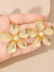 Close-up of gold floral stud earrings with pearl centres resting in an open palm showing petal texture detail