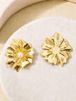 Front and back view of gold-plated floral stud earrings with faux pearl centre on a white stone surface