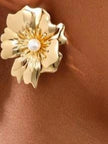 Gold floral stud earring with pearl centre worn on a model's ear against a warm brown background