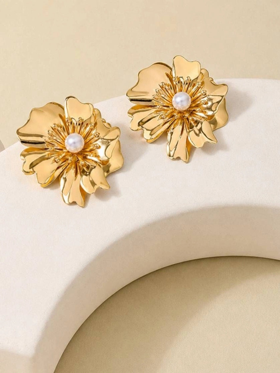 Pair of gold-plated layered petal stud earrings with pearl centres displayed on a curved white prop