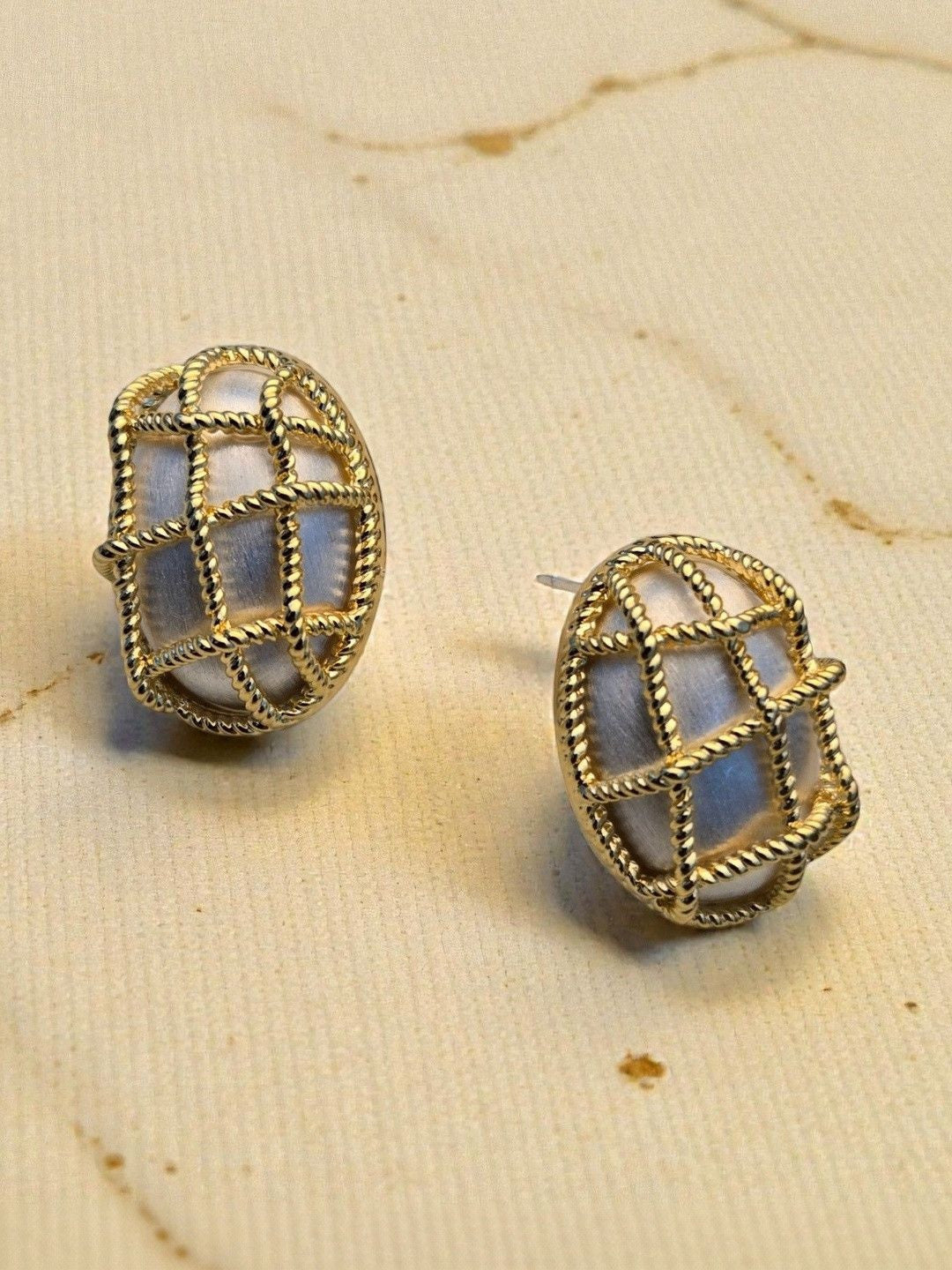 Pair of gold-plated twisted rope cage oval stud earrings on a cream fabric surface
