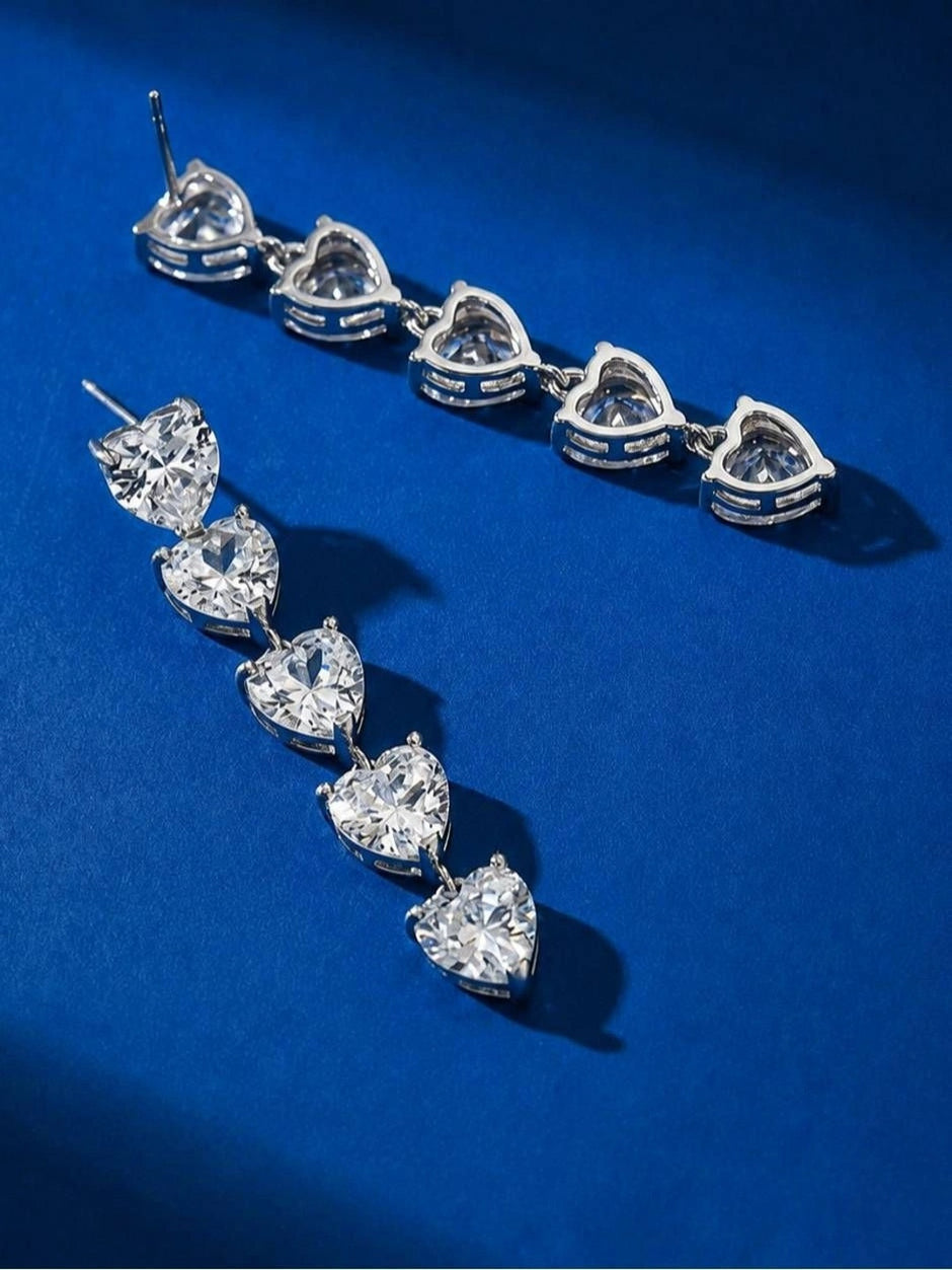 Two silver-finish heart drop earrings laid flat on a royal blue surface, showing the back and front side by side