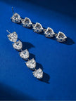 Two silver-finish heart drop earrings laid flat on a royal blue surface, showing the back and front side by side
