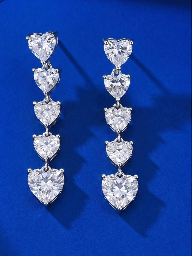 Pair of five-heart cascading CZ drop earrings displayed front-facing on a blue velvet surface