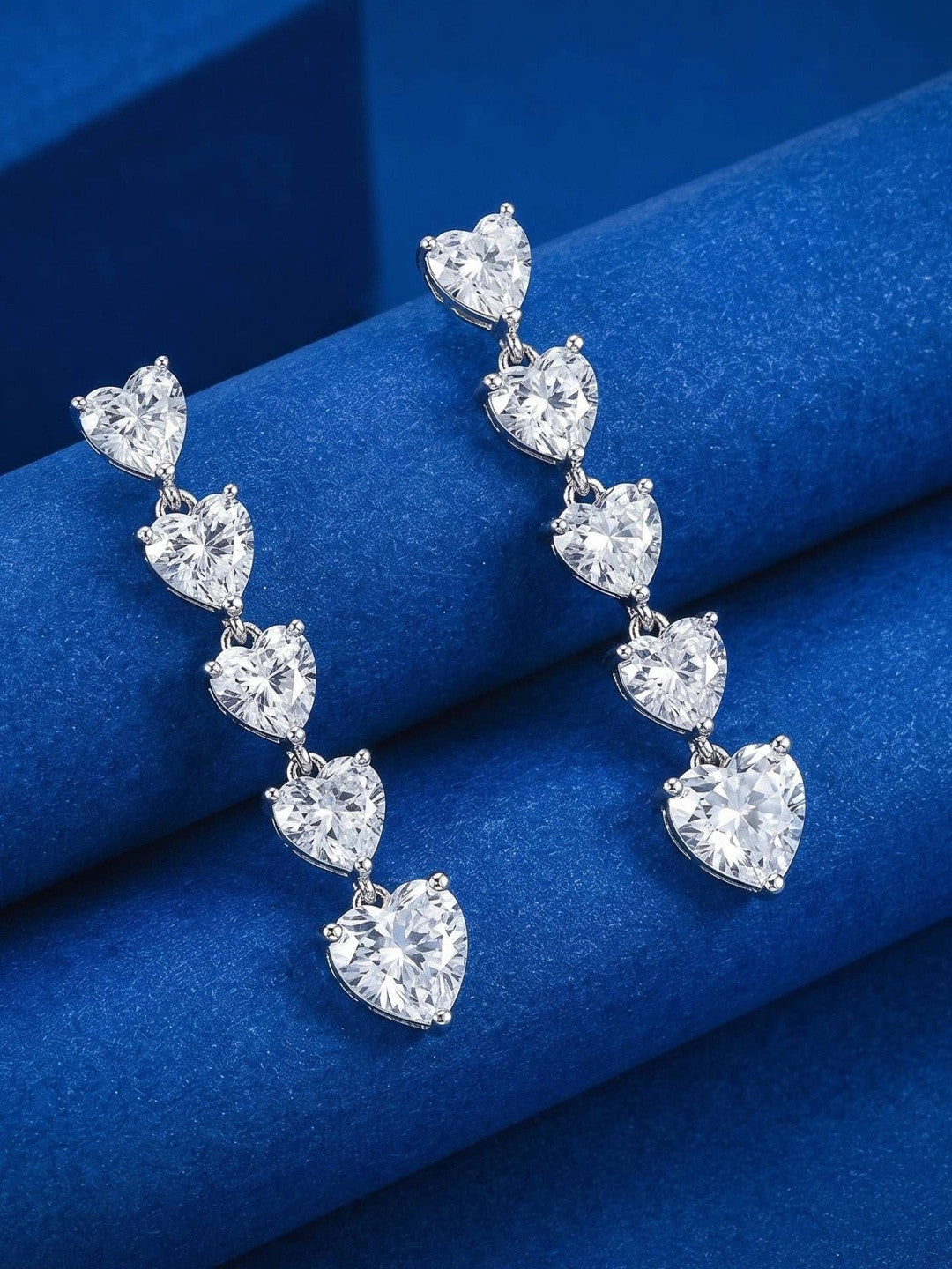 Silver heart drop earrings resting on folded blue velvet, highlighting the graduating stone sizes
