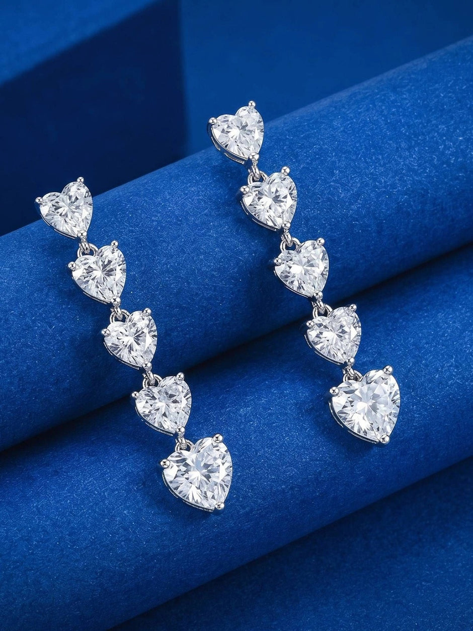 Silver heart drop earrings resting on folded blue velvet, highlighting the graduating stone sizes
