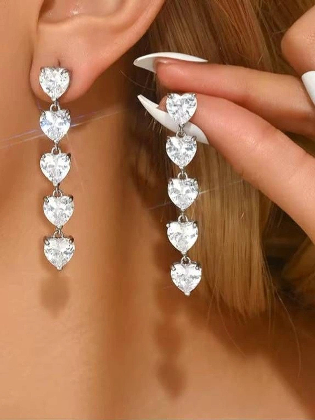 Model wearing silver cascading heart drop earrings, one earring in ear and one held up to show length