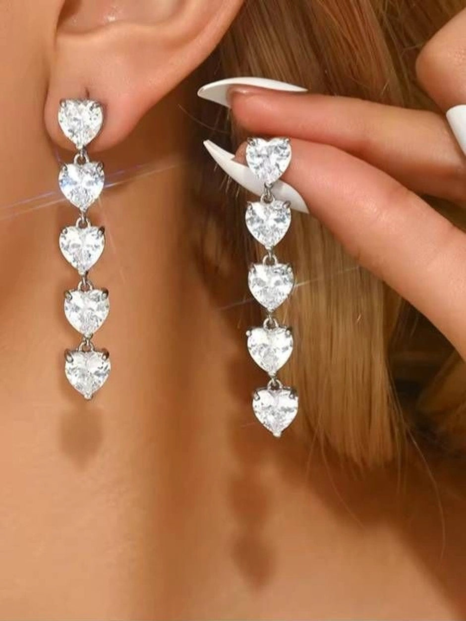 Model wearing silver cascading heart drop earrings, one earring in ear and one held up to show length