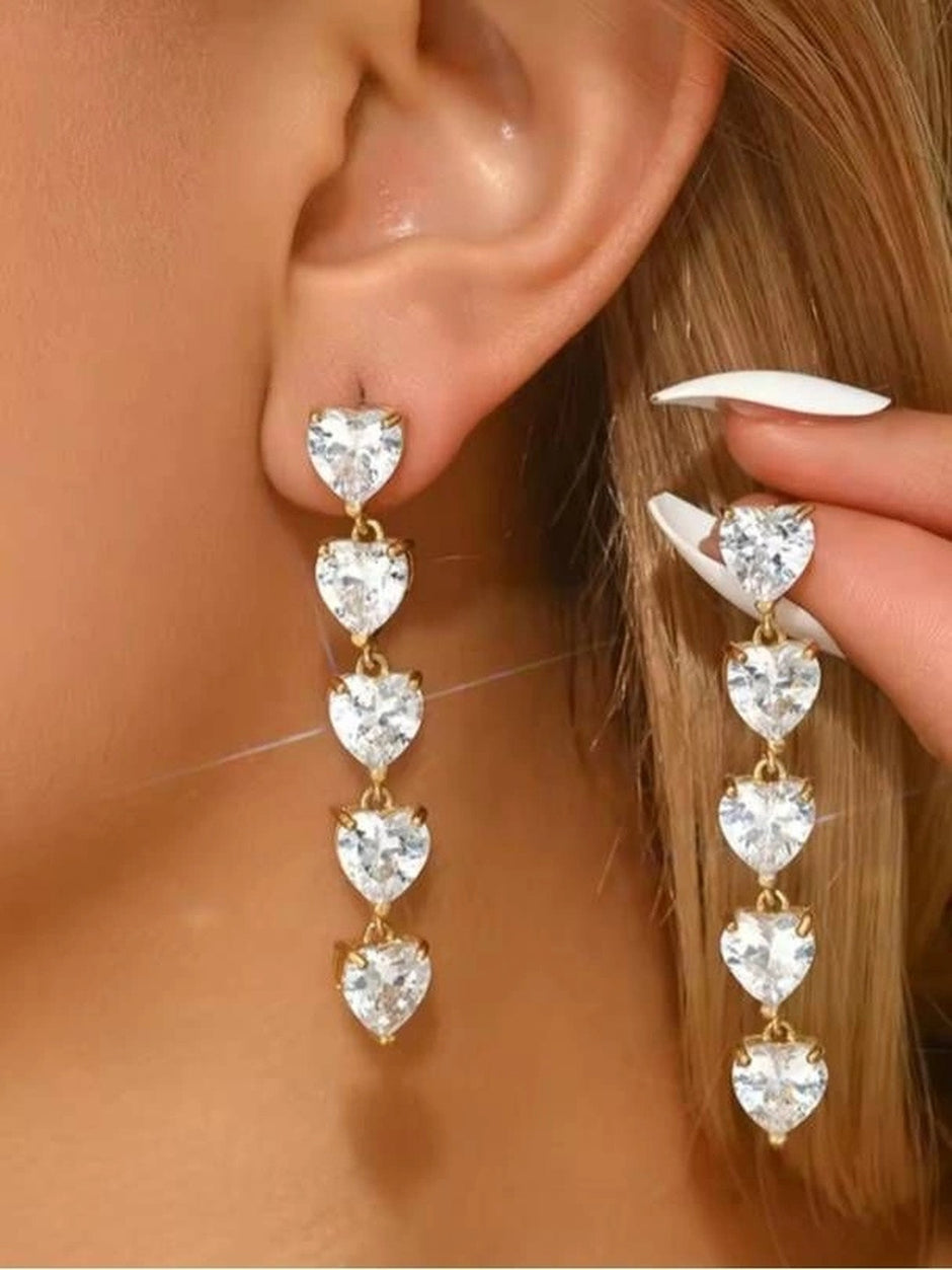 Gold-plated heart CZ drop earrings worn on a model's ear, showing full length cascade of five clear crystal hearts