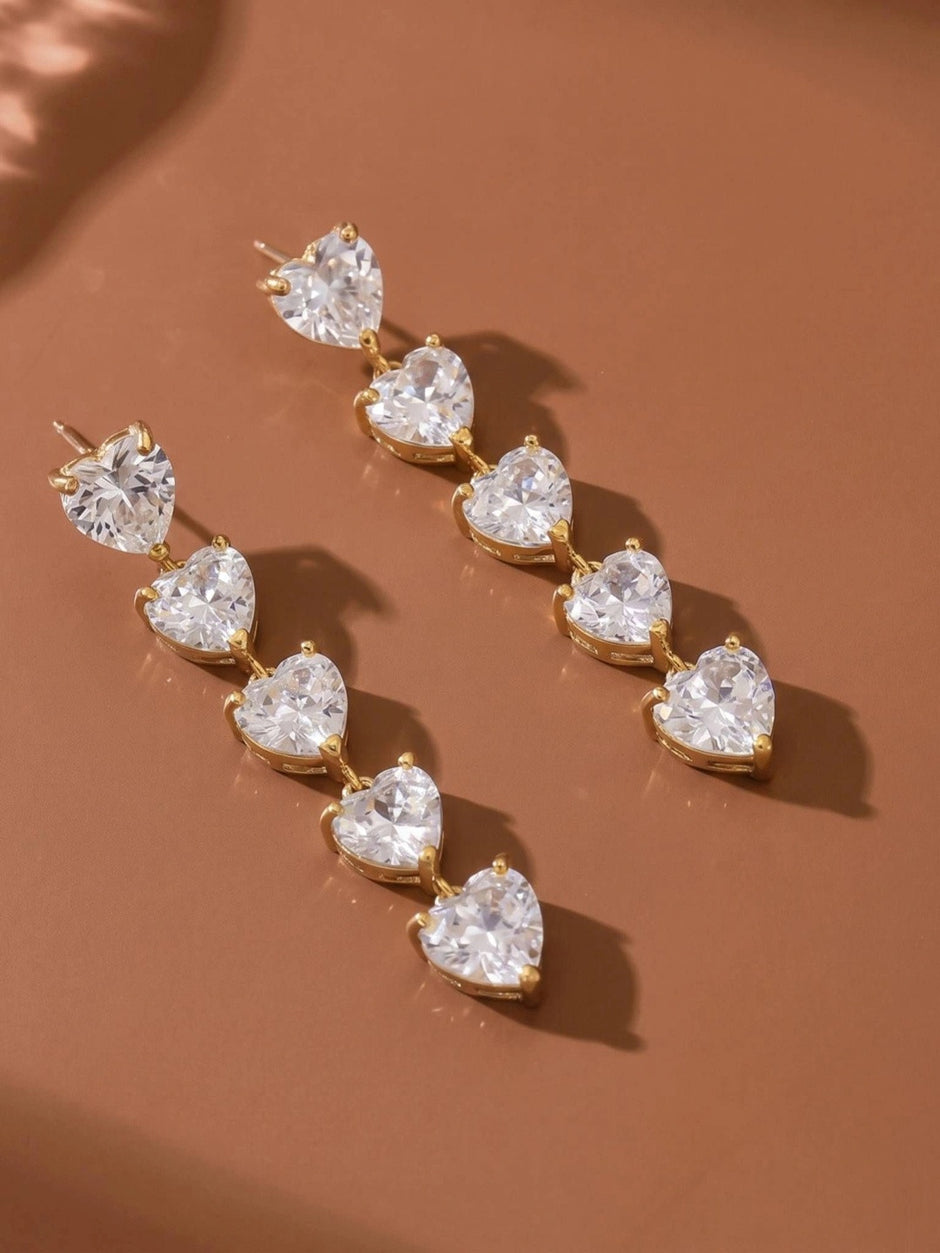 Pair of heart CZ drop earrings laid flat on a terracotta surface, showing front face of both earrings side by side