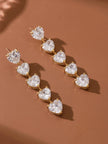 Pair of heart CZ drop earrings laid flat on a terracotta surface, showing front face of both earrings side by side