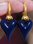 Close-up of two navy blue enamel heart drop earrings held between fingers against dark background