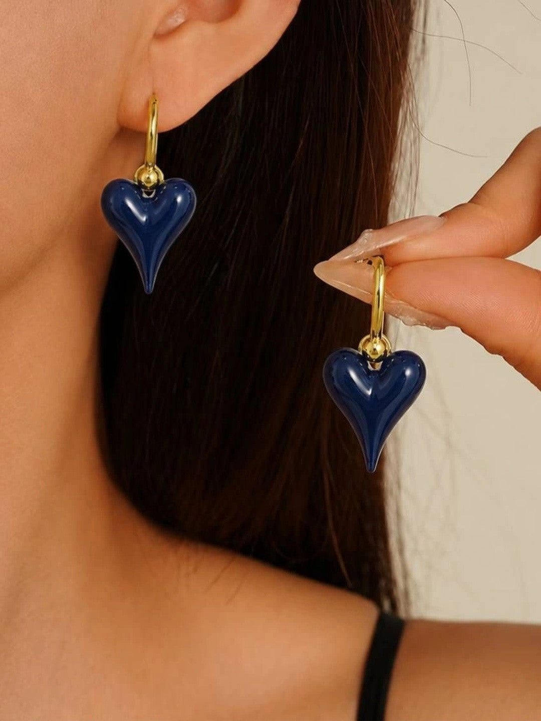 Model wearing navy blue enamel heart drop hoops on both ears with dark hair