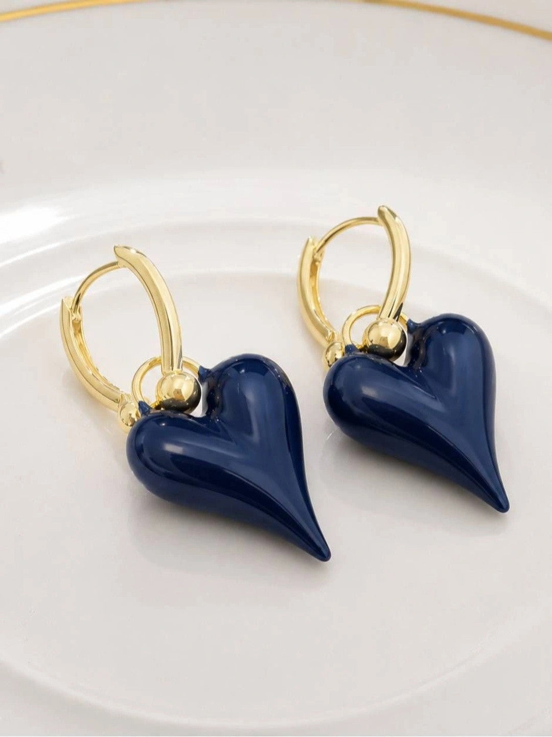 Navy blue enamel heart drop hoop earrings laid flat on white ceramic plate