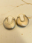 Close-up of two matte gold disc hoop earrings on a beige paper surface showing brushed texture