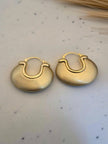Pair of matte gold chunky disc hoops placed on a white speckled marble surface near dried grass