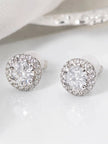 Pair of silver-finish CZ halo stud earrings with round solitaire centre and pavé surround, on white surface